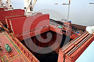 Loading coal from cargo barges onto a bulk carrier using ship cranes and grabs at the port of Muara Pantai, Indonesia. January,202