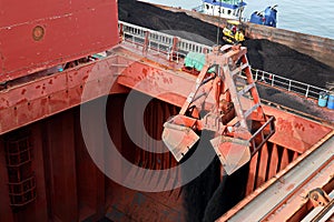 Loading coal from cargo barges onto a bulk carrier using ship cranes and grabs at the port of Muara Pantai, Indonesia. January,202