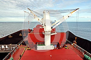 Loading coal from cargo barges onto a bulk carrier using ship cranes and grabs at the port of Muara Pantai, Indonesia. January,202