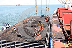 Loading coal from cargo barges onto a bulk carrier using ship cranes and grabs at the port of Muara Pantai, Indonesia. January,202