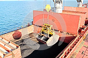 Loading coal from cargo barges onto a bulk carrier using ship cranes and grabs at the port of Samarinda, Indonesia.