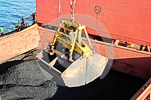 Loading coal from cargo barges onto a bulk carrier using ship cranes and grabs at the port of Samarinda, Indonesia.