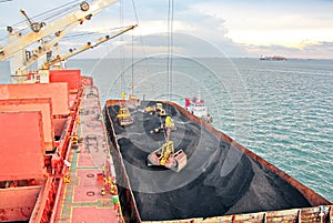 Loading coal from cargo barges onto a bulk carrier using ship cranes and grabs at the port of Samarinda, Indonesia.