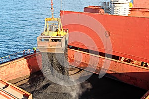 Loading coal from cargo barges onto a bulk carrier using ship cranes and grabs at the port of Samarinda, Indonesia.