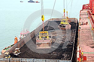 Loading coal from cargo barges onto a bulk carrier using ship cranes and grabs at the port of Samarinda, Indonesia.