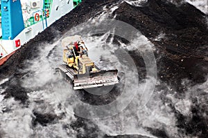 Loading coal from cargo barges onto a bulk carrier using ship cranes and grabs at the port of Samarinda, Indonesia.