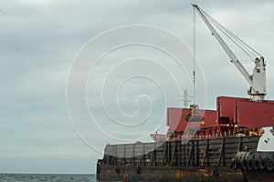 Loading coal from cargo barges onto a bulk vessel using ship cranes.