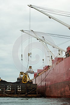 Loading coal from cargo barges onto a bulk vessel using ship cranes.