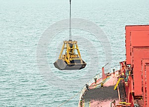 Loading coal from cargo barges onto a bulk vessel using ship cranes.