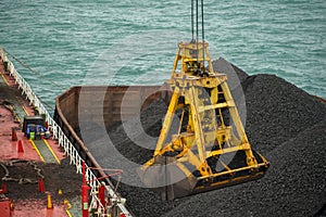 Loading coal from cargo barges onto a bulk vessel using ship cranes  in offshore coal cargo terminal.