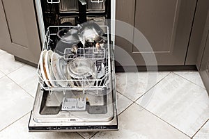 Loading the dishwasher with dirty dishes. Cups, plates, spoons, forks, pots and pans