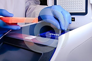 Loading a DNA tube into a PCR polymerase chain reaction thermocycler machine in a bioscience laboratory. Concept of science,
