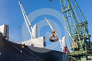 Loading dry cargo ship by cranes in port. Loading into holds of sea cargo vessel