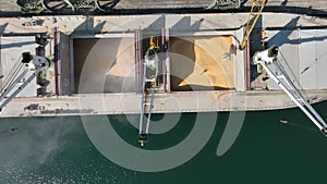 Loading dry cargo ship of wheat by cranes in port.