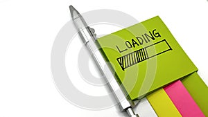 Loading message on green sticky note, with silver pen and colorful note pads, isolated on white background,