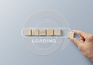 Loading, reboot, refresh or mindset concept. Hand putting wooden blocks in progress bar on gray background with the word LOADING