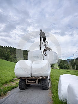 loading white grass rolls on country road in norway