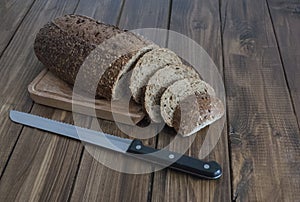 Loaf of black bread with a knife on a wooden board