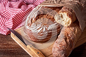 Loaf of bread, baguette and pastry on wooden table top with sharp kitchen knife