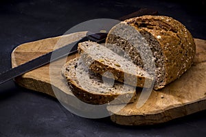 Loaf of bread with knife on wooden board. Dark background