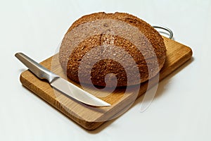 Loaf of bread with knife on wooden cutting board on white background