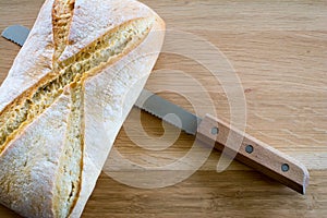 Loaf of bread and knife on wooden oak table top.