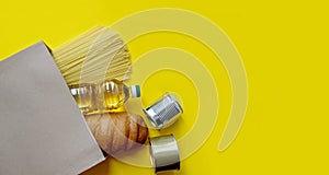 A loaf of bread, pasta, sunflower oil and cans in a paper bag on a yellow isolated background. Food delivery, donation, banner.