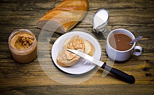 A loaf of bread and a sandwich piece of bread with peanut butter and knife, Cup and milk jug on