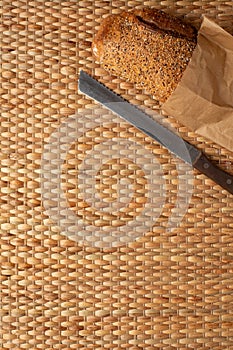 A loaf of bread on weave grass background with knife showing texture.