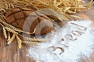 A loaf of bread and wheat ears on wooden background with flour