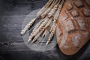 Loaf of crusty brown bread golden wheat rye ears on wood board