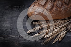 Loaf of fresh-baked brown bread wheat rye ears on wooden board