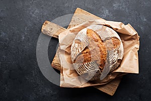 A loaf of fresh dark round buckwheat bread from a private bakery on a dark background on a vintage wooden cutting board