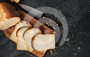 Loaf of fresh sliced white bread laid out on a cutting board and a sharp knife nearby. Top view with copy space  bread crumbs on