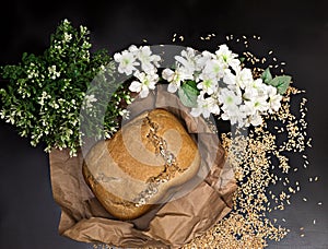 A loaf of homemade rye bread on a background of scattered grains and flowers, freshly baked bread on rough paper, home cooking,