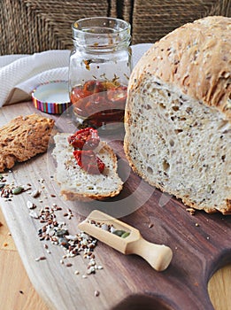 loaf of homemade whole grain bread and a cut slice of bread on a wooden cutting board. A mixture of seeds and whole