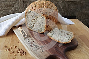 loaf of homemade whole grain bread and a cut slice of bread on a wooden cutting board. A mixture of seeds and whole