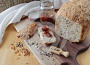 loaf of homemade whole grain bread and a cut slice of bread on a wooden cutting board. A mixture of seeds and whole