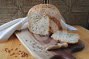 loaf of homemade whole grain bread and a cut slice of bread on a wooden cutting board. A mixture of seeds and whole