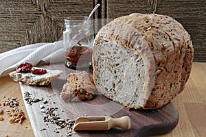 loaf of homemade whole grain bread and a cut slice of bread on a wooden cutting board. A mixture of seeds and whole