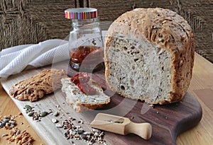 loaf of homemade whole grain bread and a cut slice of bread on a wooden cutting board. A mixture of seeds and whole