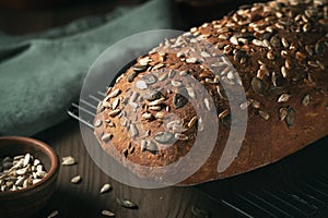 Loaf of homemade whole grain bread with seeds cool down on a wire rack on a wooden table