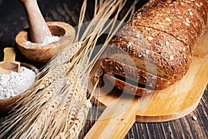 loaf of rye bread, ears of wheat and a bowl of flour. Close-up