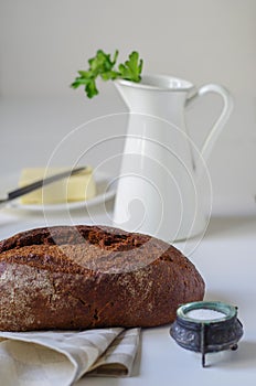 Loaf of rye bread on linen napkin with salt, butter and white jug