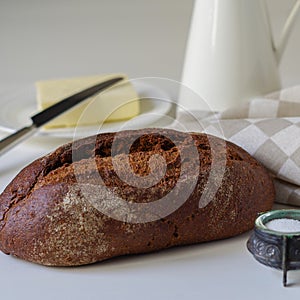 Loaf of rye bread on white table with salt, butter and jug