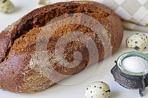 Loaf of rye bread on white table with salt and quail eggs