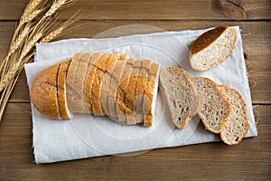 A loaf of wheat bread with bran is cut into slices and lies on a linen napkin.