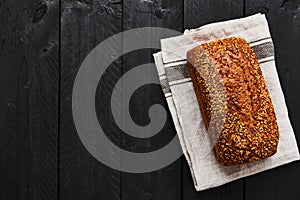 Loaf of whole wheat bread on gray dishtowel over black wooden ta