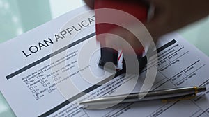 Loan application document pending, hand stamping seal on official paper, closeup