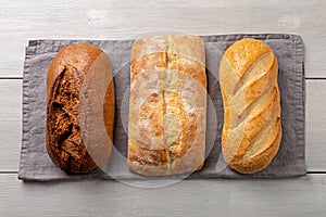 Loaves of fresh hommade whole bread on gray napkin flat lay on white wooden background